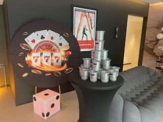 Décor sur le thème du casino avec une grande image de machine à sous, un dé géant, une pyramide de seaux argentés sur une table haute et une affiche de film James Bond en arrière-plan.